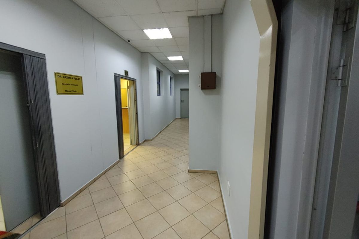 A commercial hallway featuring ceramic tile flooring, suspended ceiling with recessed lighting, and multiple access doors to office or clinic suites.