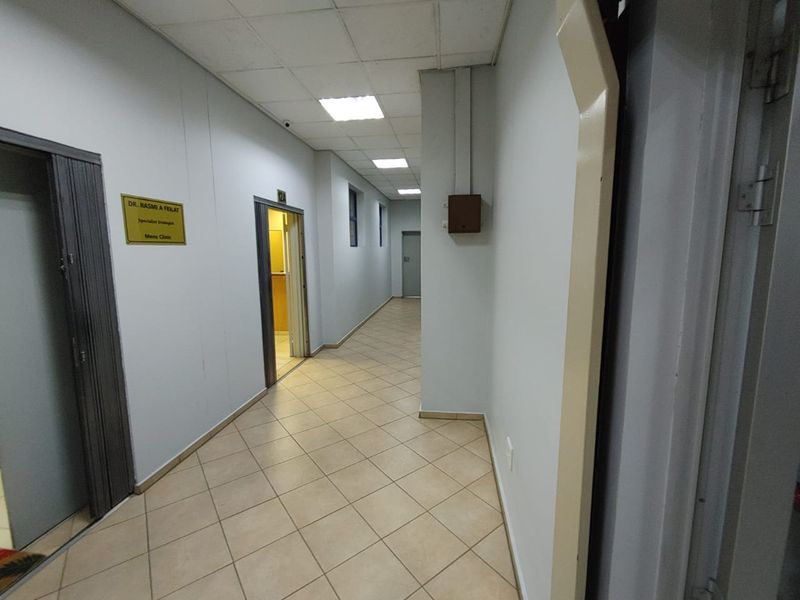 A commercial hallway featuring ceramic tile flooring, suspended ceiling with recessed lighting, and multiple access doors to office or clinic suites.