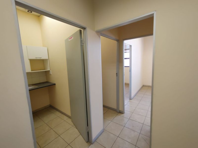 A functional commercial hallway providing access to multiple rooms, including a small kitchenette area with built-in cabinetry and tiled flooring throughout.