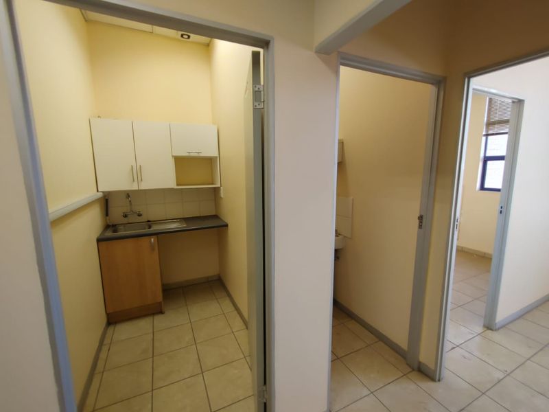 A functional scullery or kitchenette area featuring built-in cabinetry, a stainless steel sink, and tiled flooring, adjacent to additional office or utility rooms.