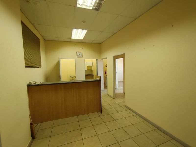 Empty commercial office space featuring a built-in reception counter, tiled flooring, and suspended ceiling with recessed lighting, ready for custom fit-out.