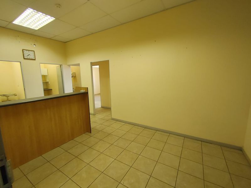 An empty commercial office space featuring a built-in reception counter, tiled flooring, and a suspended ceiling with recessed lighting.