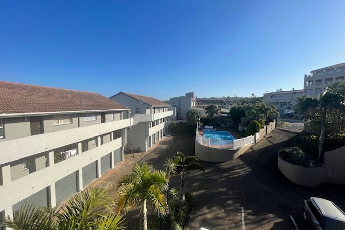An elevated aerial view of the apartment complex grounds, featuring a communal swimming pool, landscaped garden areas, and designated parking facilities.
