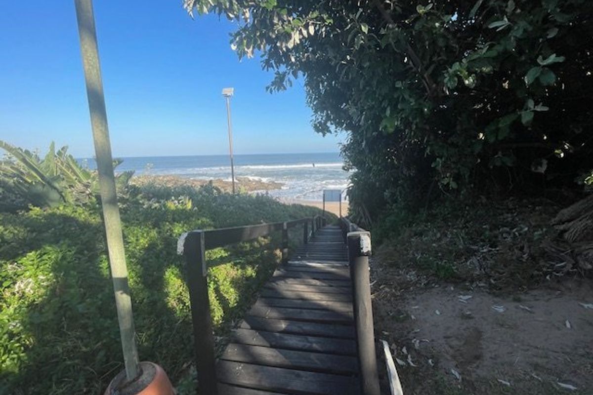 A wooden staircase providing direct access to the beach, surrounded by coastal vegetation and offering ocean views.