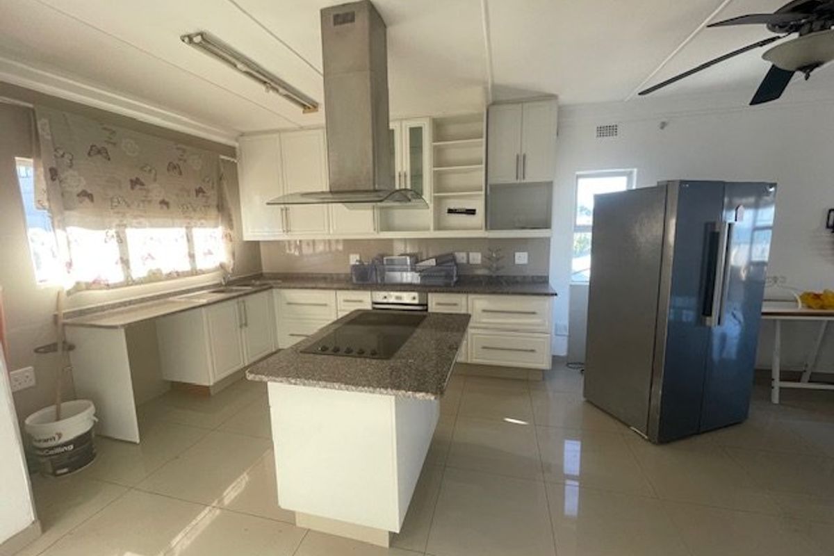 Spacious kitchen featuring a central island, granite countertops, stainless steel extractor fan, and ample built-in cabinetry with tiled flooring throughout.