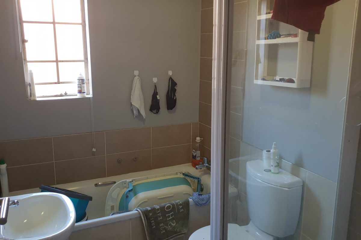 A functional bathroom featuring a bathtub, shower enclosure, toilet, and pedestal basin with neutral wall tiling and natural light from a window.