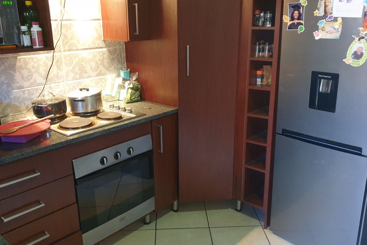 A functional kitchen featuring dark wood cabinetry, granite countertops, a built-in oven, electric hob, and tiled flooring.