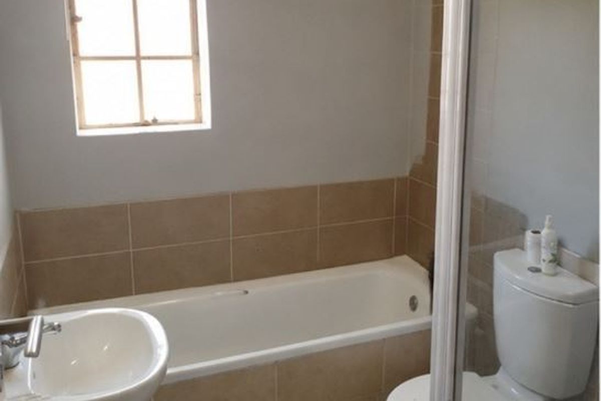 A functional bathroom featuring a bathtub, pedestal basin, and toilet with neutral wall tiling and natural light from a window.