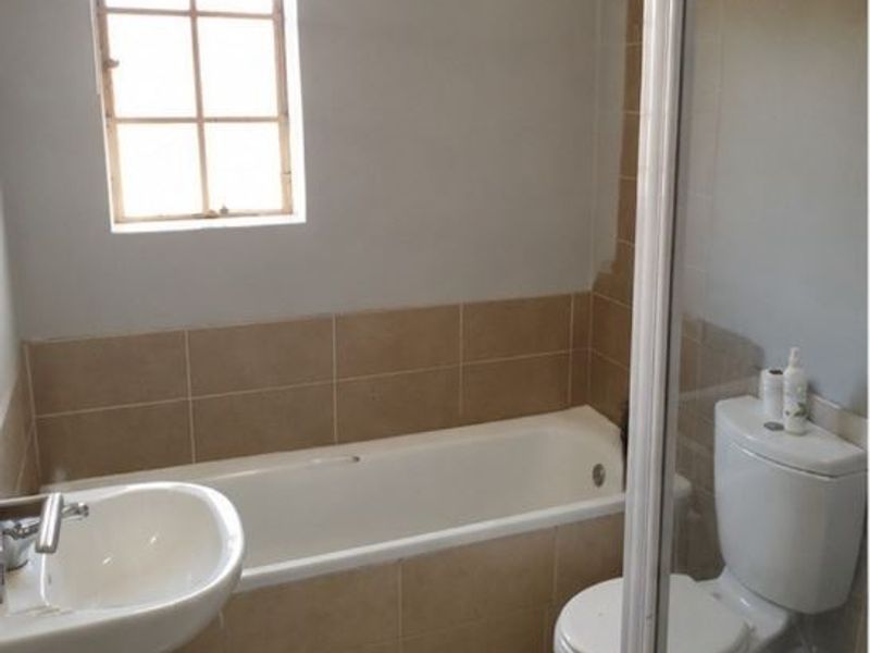 A functional bathroom featuring a bathtub, pedestal basin, and toilet with neutral wall tiling and natural light from a window.