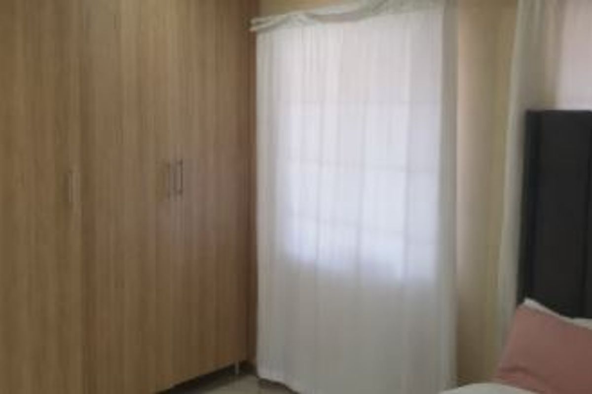 A bedroom featuring light wood-finish built-in cupboards and a window with sheer curtains.