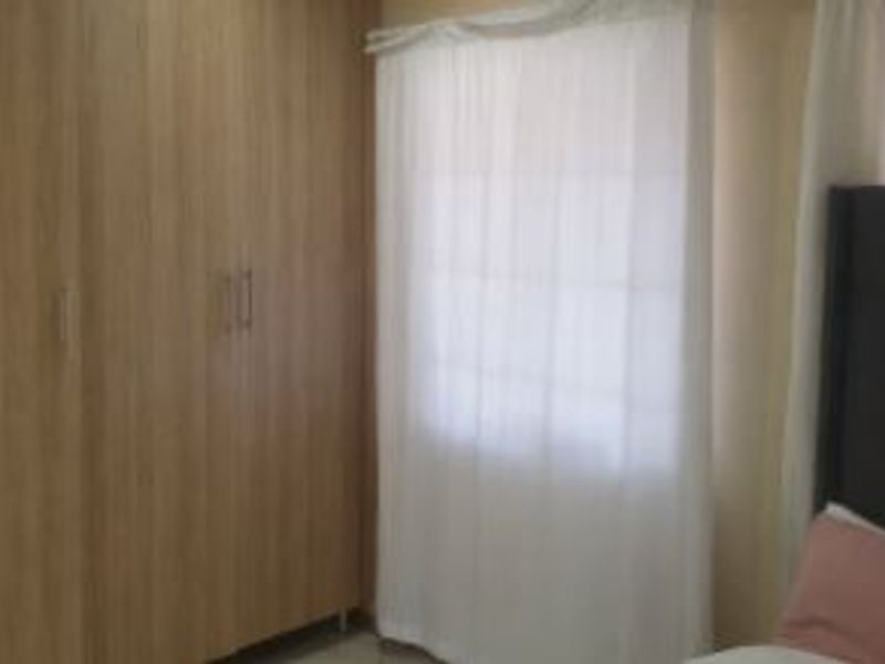 A bedroom featuring light wood-finish built-in cupboards and a window with sheer curtains.