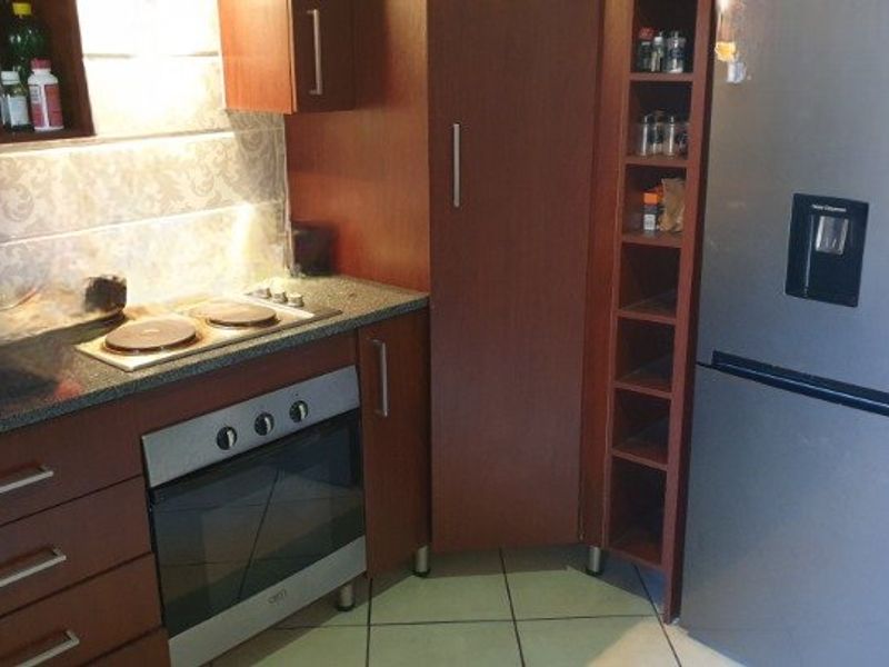 Compact kitchen featuring dark wood cabinetry, granite countertops, built-in oven, electric hob, and tiled flooring.