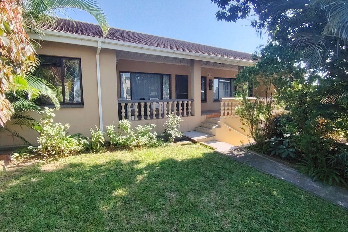Rear view of the house featuring a covered patio with concrete balustrades, a paved walkway, and a well-maintained garden area.