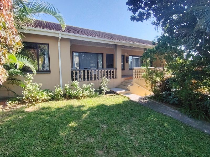 Rear view of the house featuring a covered patio with concrete balustrades, a paved walkway, and a well-maintained garden area.