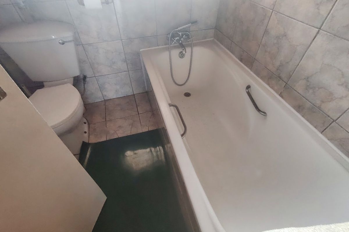 A functional bathroom featuring a standard bathtub with shower mixer and a toilet, finished with dated wall and floor tiling.