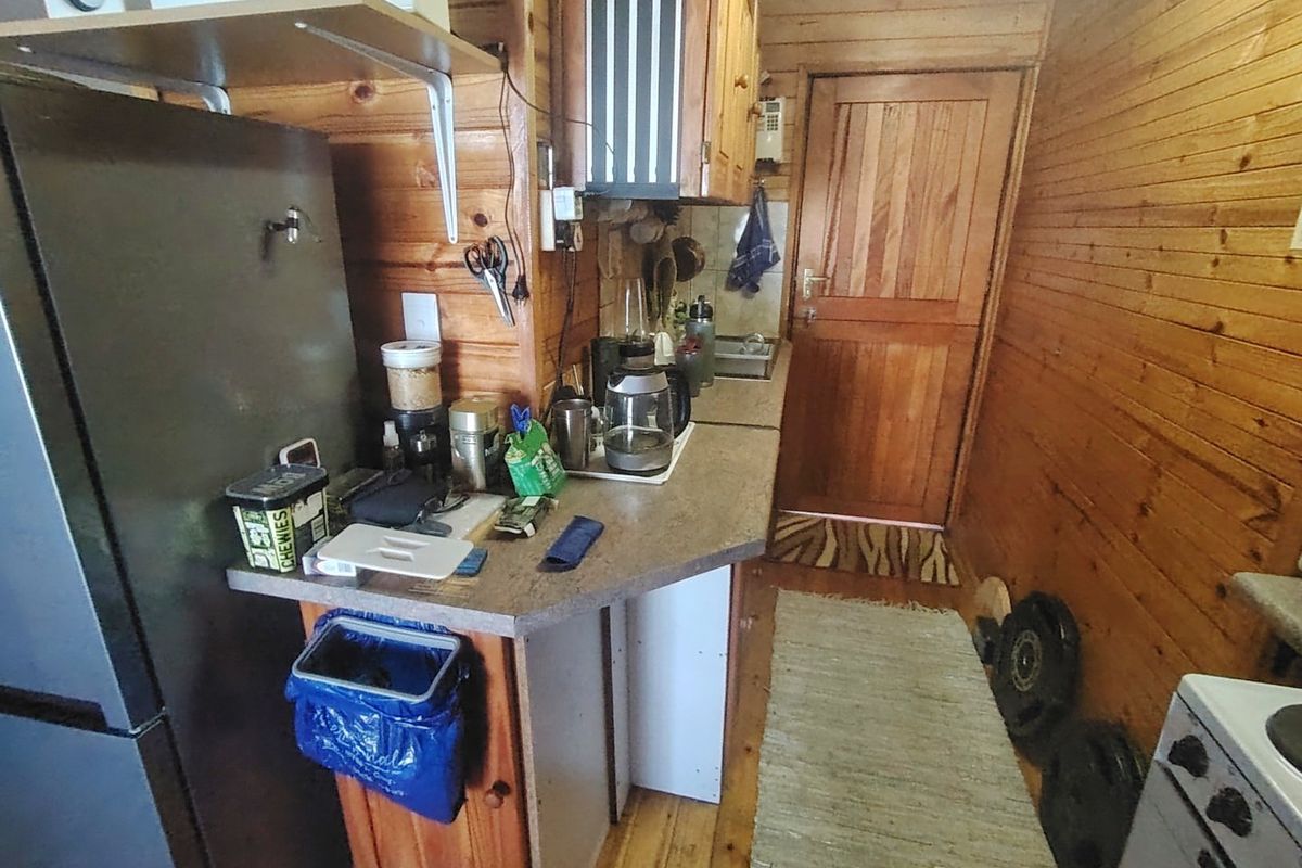 A compact kitchen featuring wooden wall paneling, wooden cabinetry, and a laminate countertop, providing a rustic aesthetic with functional built-in fixtures.