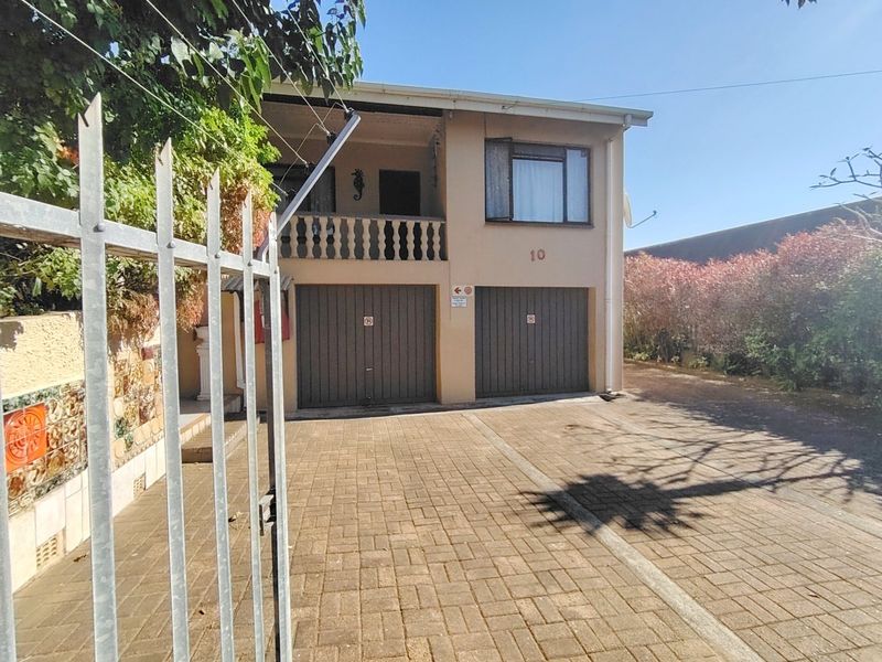 Front view of a two-story house featuring a double garage, paved driveway, and an upper-level balcony with a balustrade.