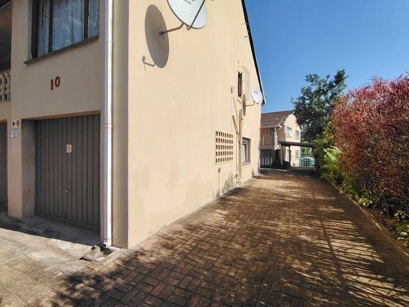 Side view of the property showing a paved driveway, garage entrance, and exterior wall with mounted satellite dishes.