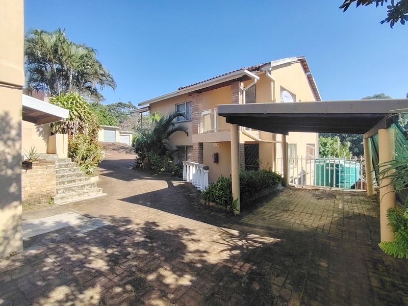 Exterior view of the property featuring a paved driveway, covered carport, and multi-level access with stairs and a balcony.