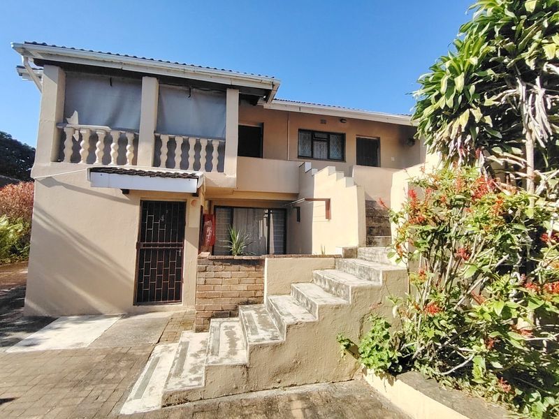 Rear exterior view of the property featuring a concrete staircase, a balcony with balustrades, and a brick retaining wall in a weathered condition.