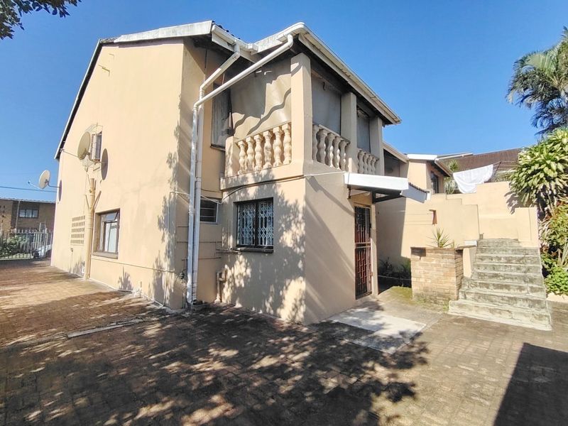 Rear exterior view of the property featuring a paved courtyard, an external staircase, and a balcony with a decorative balustrade.
