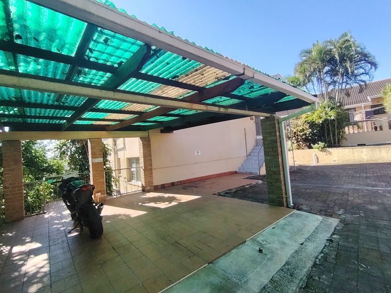 A covered carport area featuring brick pillars and tiled flooring, with an adjacent external staircase leading to the upper level of the property.