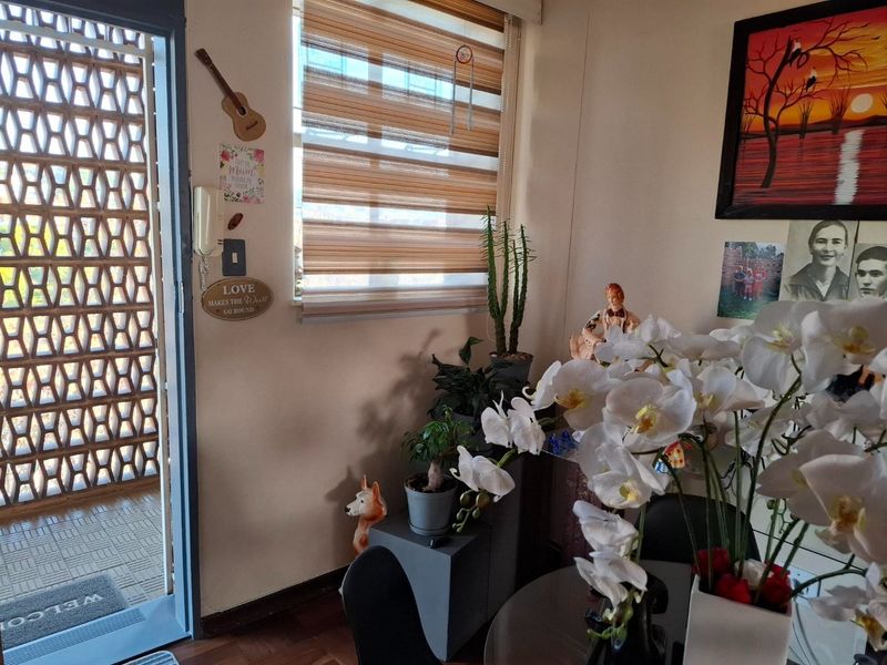 A living area featuring laminate flooring, zebra blinds, and an intercom system, with an adjacent outdoor area visible through a decorative breeze block screen.