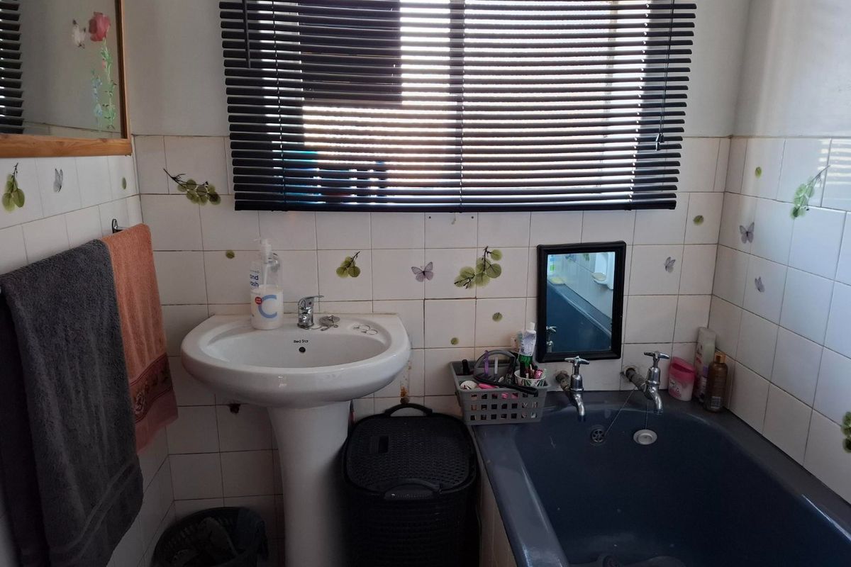 A functional bathroom featuring a pedestal washbasin, built-in bathtub, and tiled walls, offering potential for modernization and aesthetic updates.