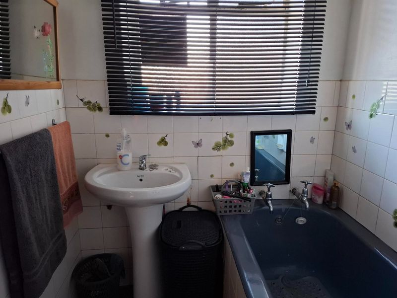 A functional bathroom featuring a pedestal washbasin, built-in bathtub, and tiled walls, offering potential for modernization and aesthetic updates.