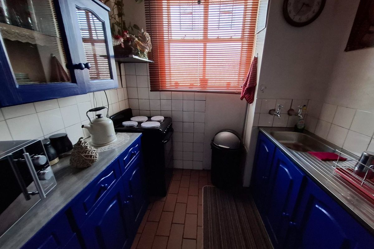 Compact kitchen featuring blue cabinetry, tiled backsplash, stainless steel sink, and a freestanding stove, offering a functional layout with potential for modern updates.