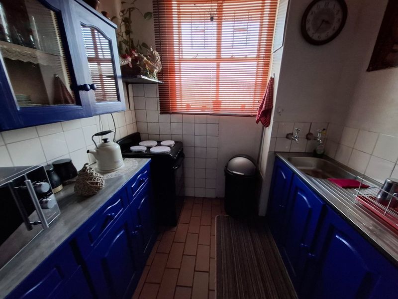Compact kitchen featuring blue cabinetry, tiled backsplash, stainless steel sink, and a freestanding stove, offering a functional layout with potential for modern updates.