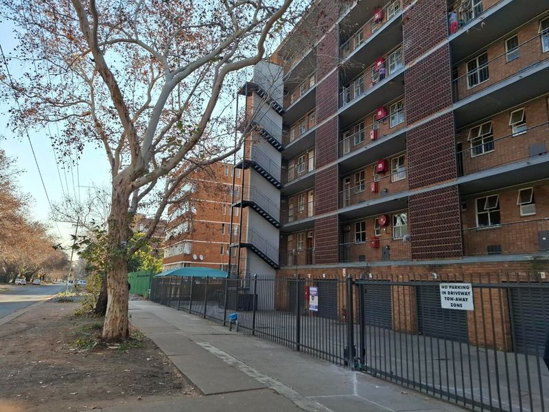 Exterior view of a multi-story brick apartment building featuring an external fire escape staircase, security fencing, and balconies.