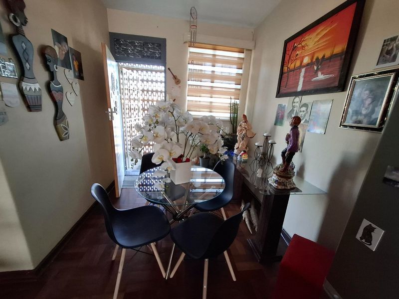 A compact dining area featuring parquet flooring, a security gate at the entrance, and adjustable roller blinds for natural light control.