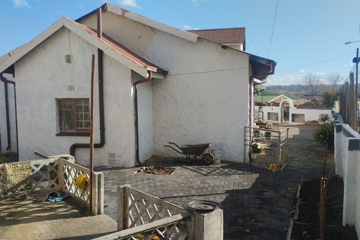 Rear exterior view of the property featuring a paved courtyard, boundary wall, and gabled roof structure with visible signs of exterior maintenance required.