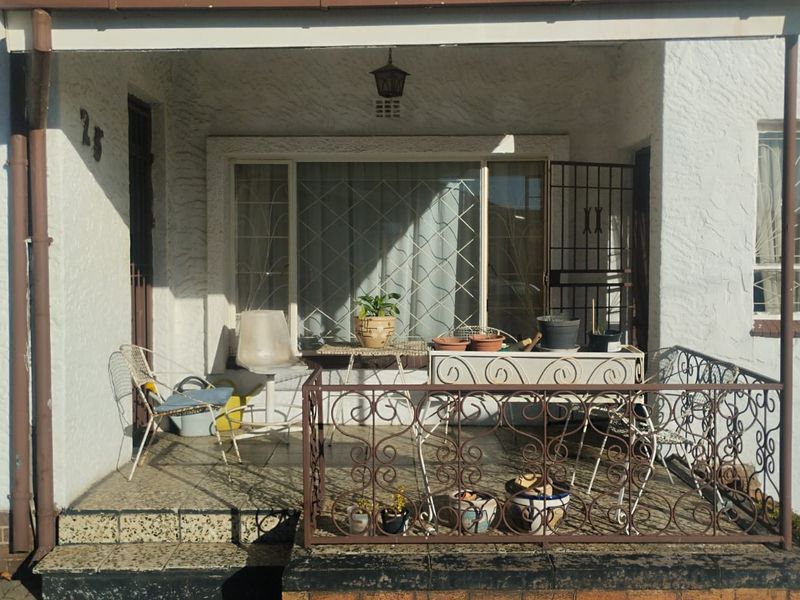 A covered front patio area featuring a wrought iron balustrade, tiled flooring, and a security gate, providing a functional outdoor entrance space.