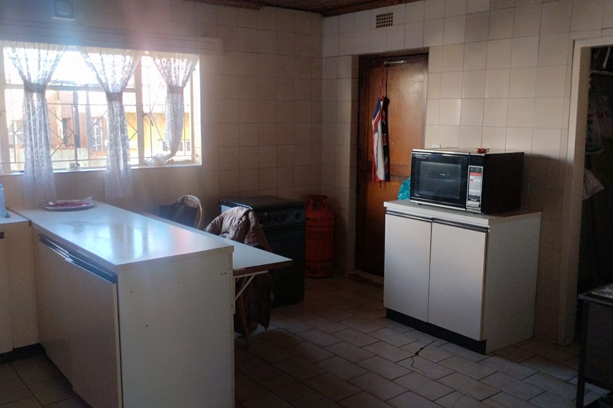 A dated kitchen featuring tiled walls and flooring, built-in cabinetry, and a sink, requiring modernization to improve functionality and aesthetic appeal.