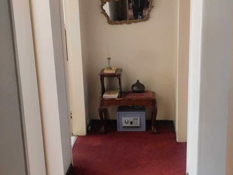 A narrow residential hallway featuring red carpet flooring and neutral wall finishes, providing access to adjacent rooms.
