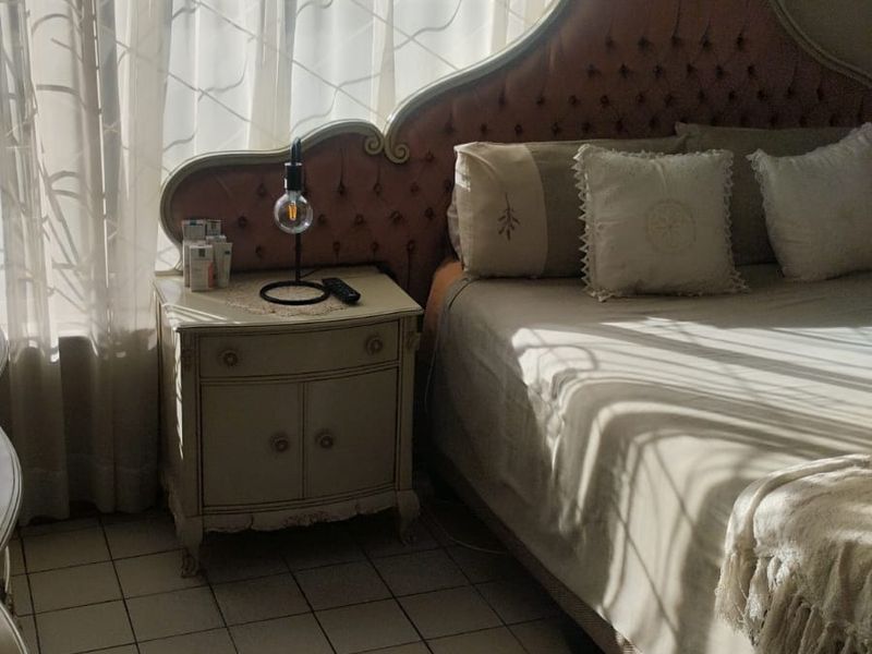 A bedroom featuring tiled flooring and large windows with curtain tracks, allowing for natural light to fill the space.