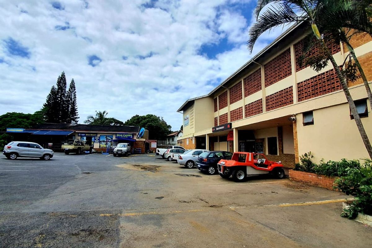 Exterior view of a commercial property featuring a paved parking area, brick facade with decorative breeze blocks, and a covered entrance walkway.