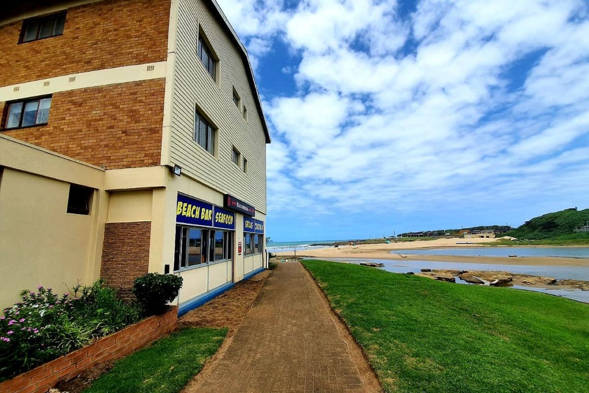 Exterior view of a commercial building featuring a brick facade and paved walkway, situated adjacent to a coastal landscape and beach area.