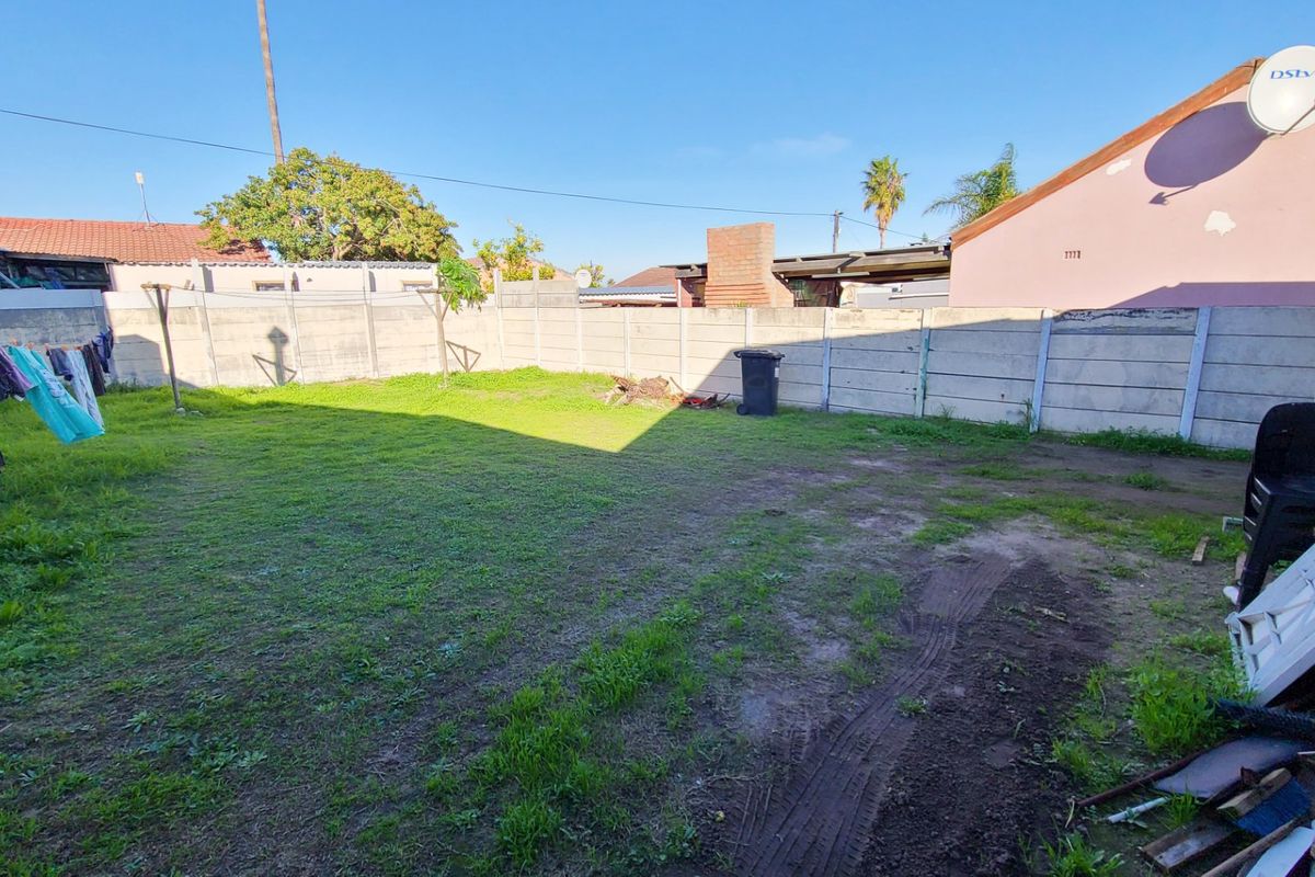 A spacious rear garden area enclosed by precast concrete boundary walls, featuring a lawn with areas of exposed soil.