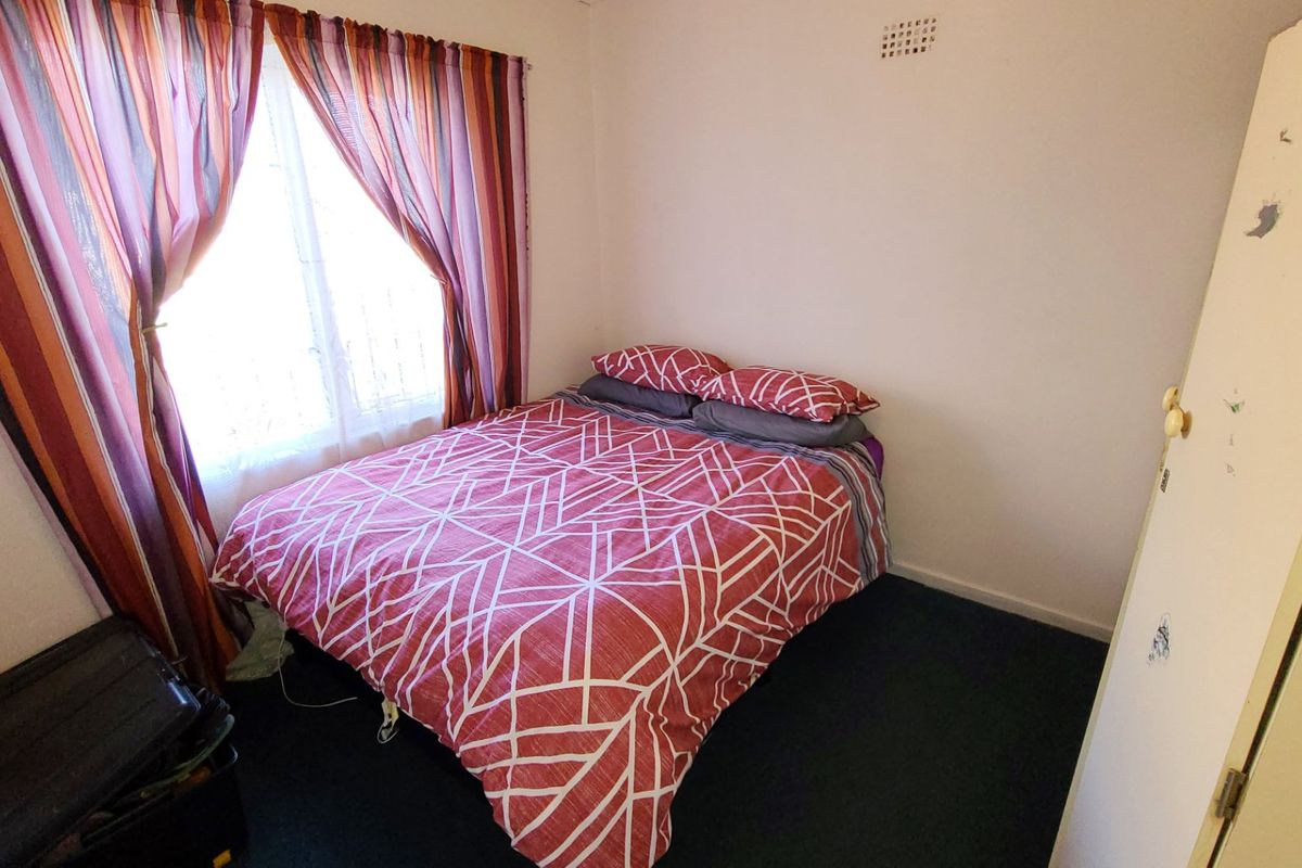 A compact bedroom featuring a window with curtains and a ceiling ventilation vent, requiring minor cosmetic updates to the door frame and finishes.