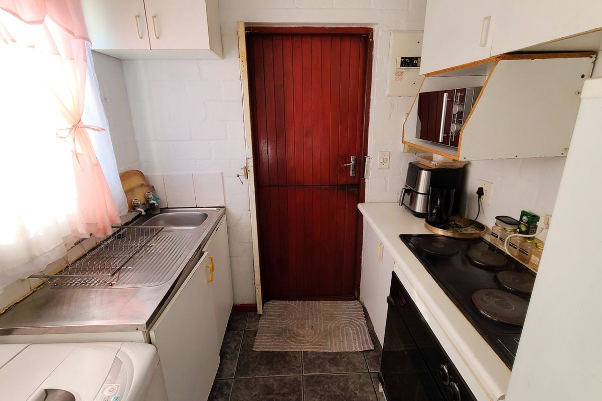 Compact kitchen featuring built-in cabinetry, stainless steel sink, electric hob, and oven, with direct access to an exterior door.