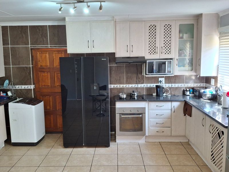 A functional kitchen featuring built-in cabinetry, granite countertops, a tiled backsplash, and integrated appliances including an oven, hob, and extractor fan.