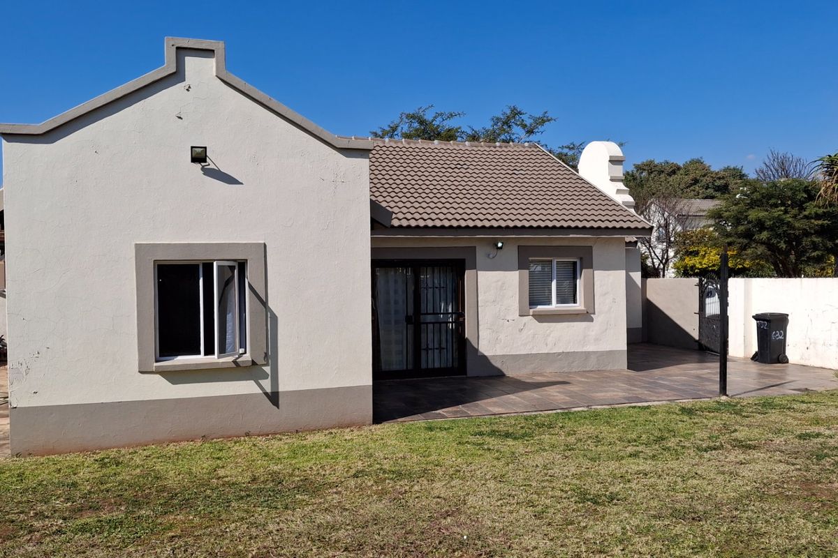 Rear view of the townhouse featuring a tiled patio, sliding glass doors with security gates, and a private garden area.