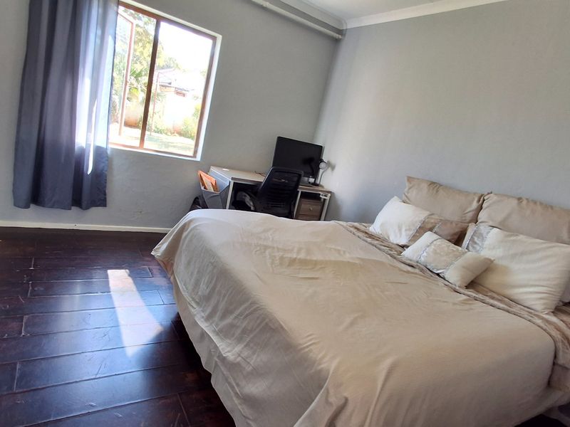A spacious bedroom featuring dark timber flooring, built-in cupboards, and neutral wall tones, offering a functional layout with natural light.