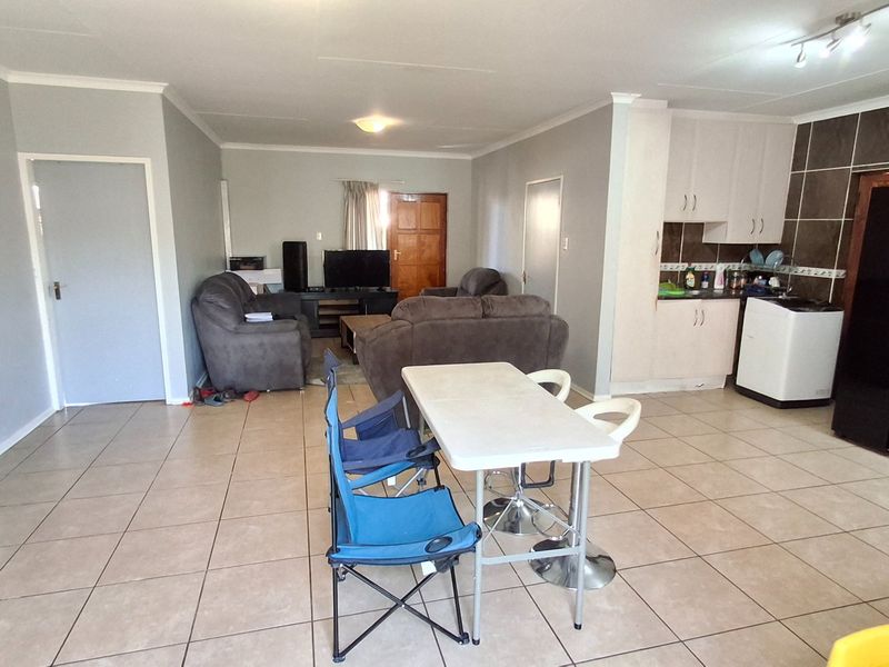 Open-plan living area featuring tiled flooring and a functional kitchen with cabinetry and tiled backsplash, creating a versatile space for living and dining.