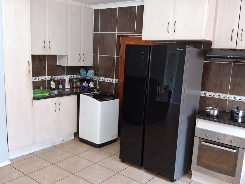 Functional kitchen featuring light-toned cabinetry, dark tiled backsplash, built-in oven with extractor fan, and tiled flooring.