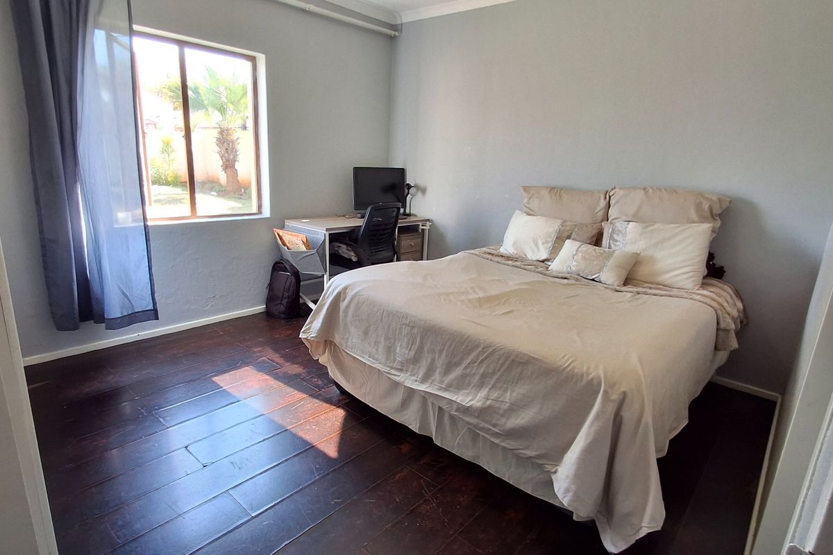 A well-lit bedroom featuring dark timber flooring, a built-in cupboard, and a window overlooking the garden area.