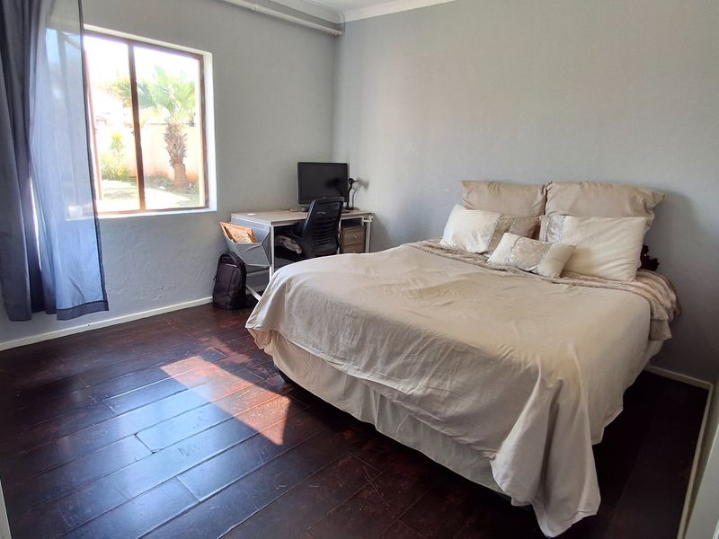 A well-lit bedroom featuring dark timber flooring, a built-in cupboard, and a window overlooking the garden area.